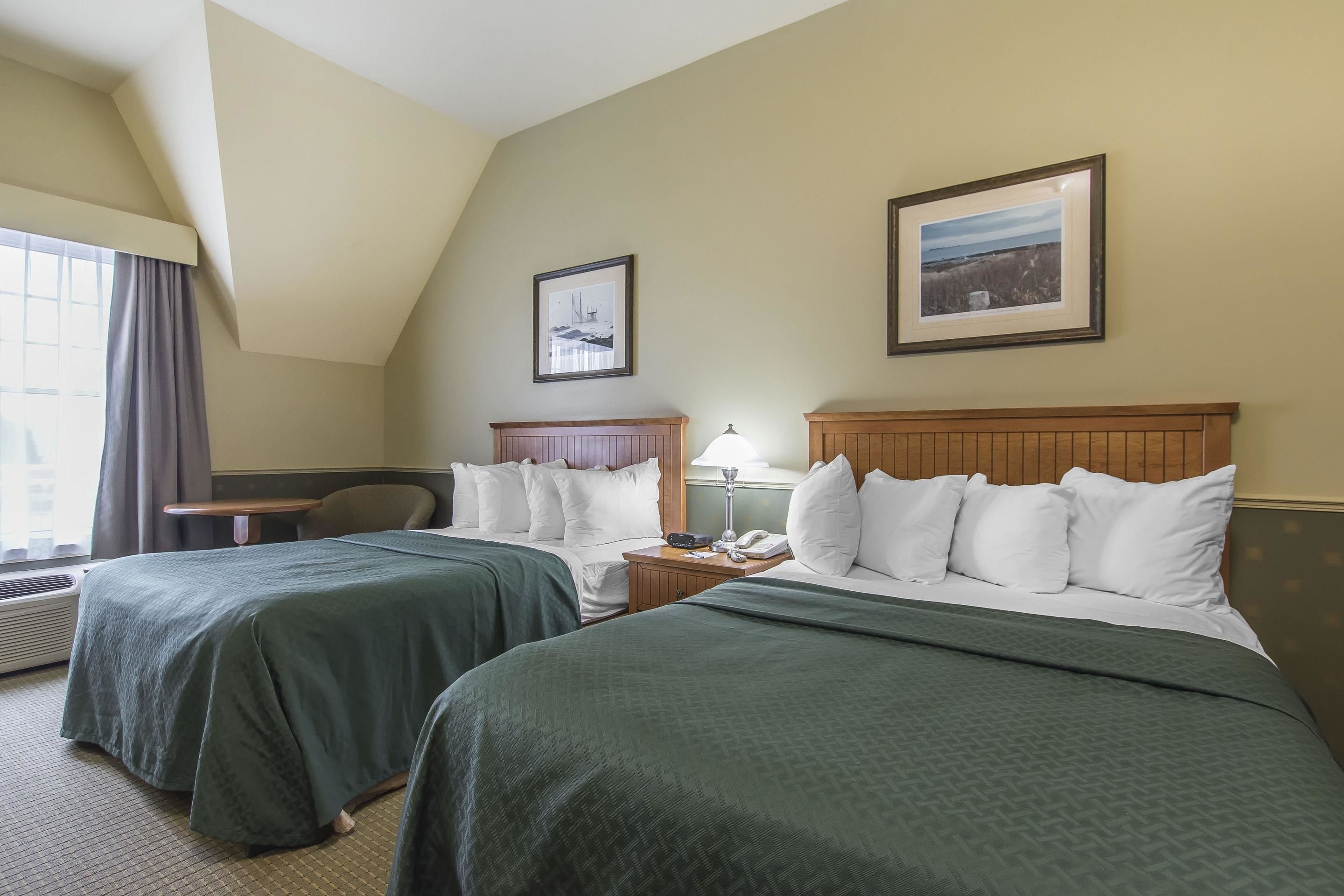 A hotel room with two beds, a desk, a chair, and two framed pictures on the wall.