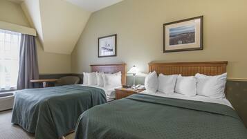 A hotel room with two beds, a desk, a chair, and two framed pictures on the wall.