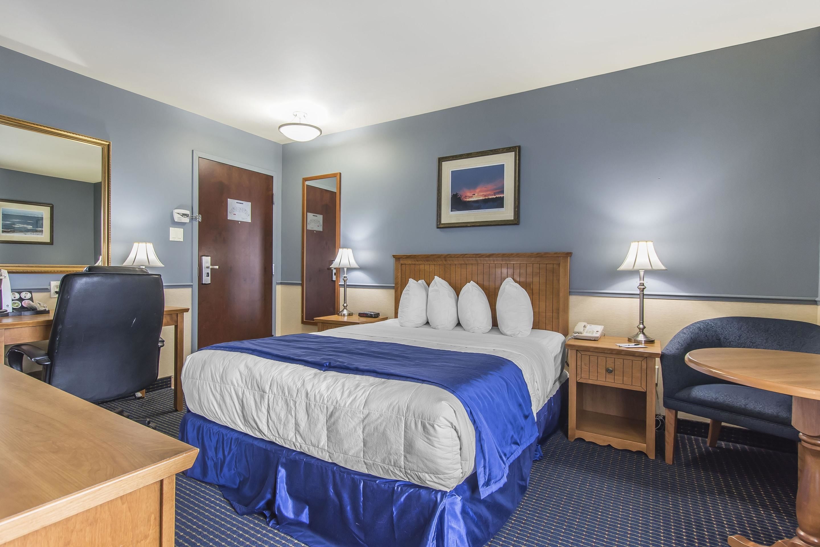 A hotel room with a bed, desk, chair, and a nightstand with lamps.