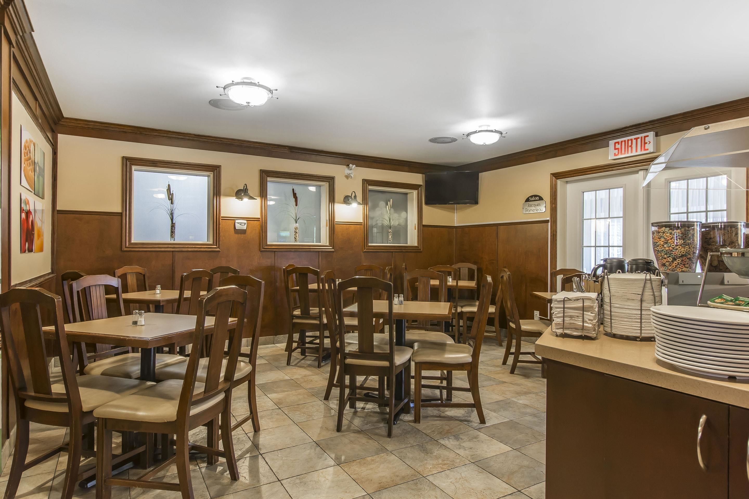 Restaurante com mesas e cadeiras de madeira, um balcão de buffet e quadros nas paredes.