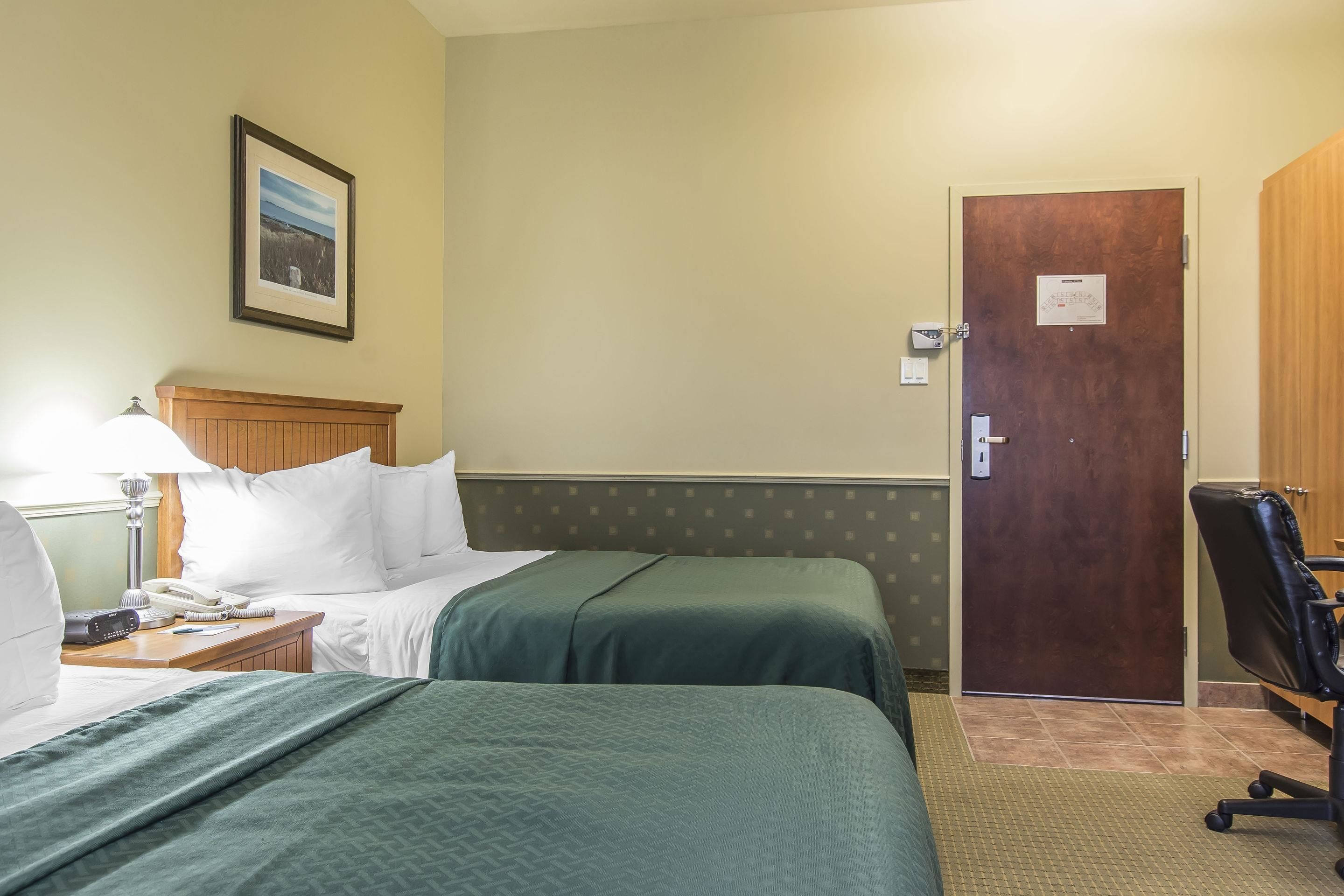 A hotel room with two beds, a wooden headboard, a desk with a lamp, a phone, and a framed picture on the wall.