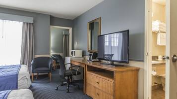 Habitación de hotel con dos camas, un escritorio con computadora, una silla, un televisor, un microondas y un baño visible a través de una puerta abierta.