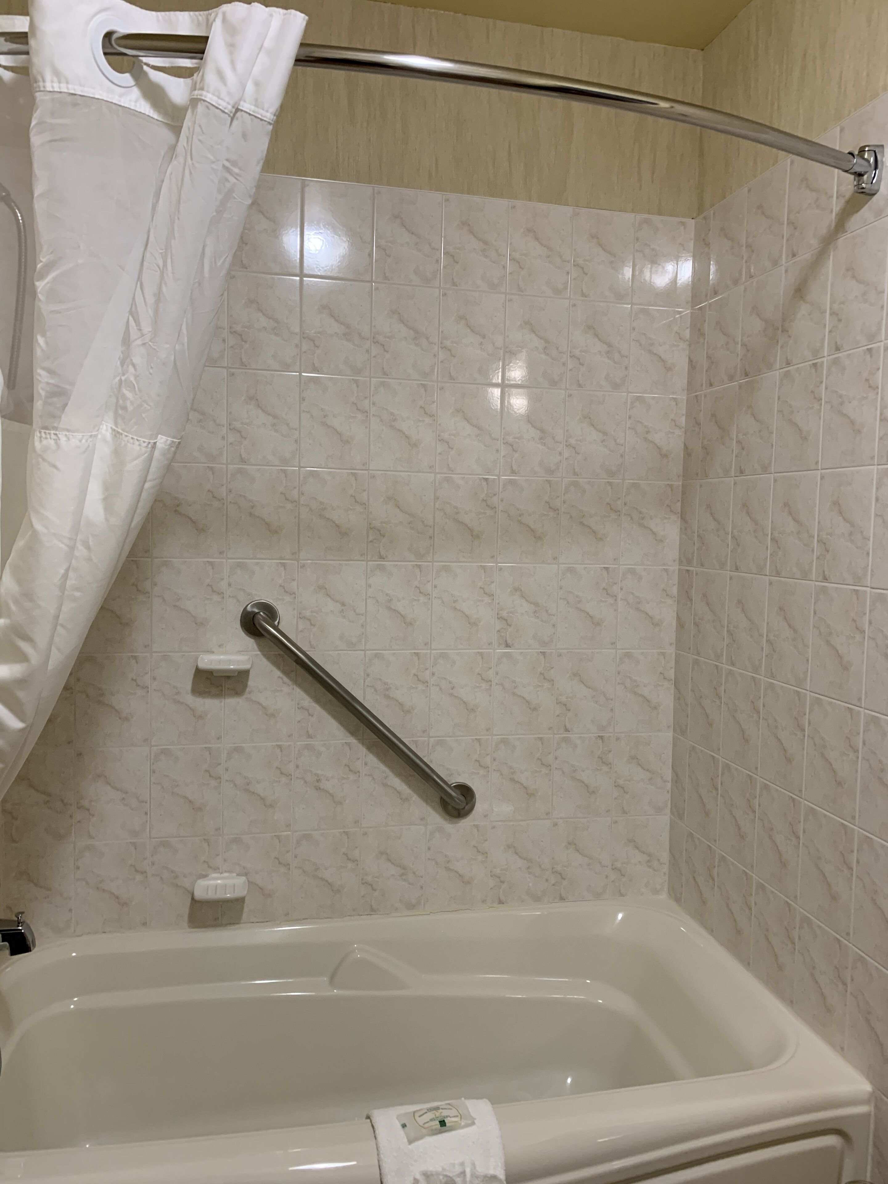 A bathroom with a bathtub, a shower curtain, and a grab bar.