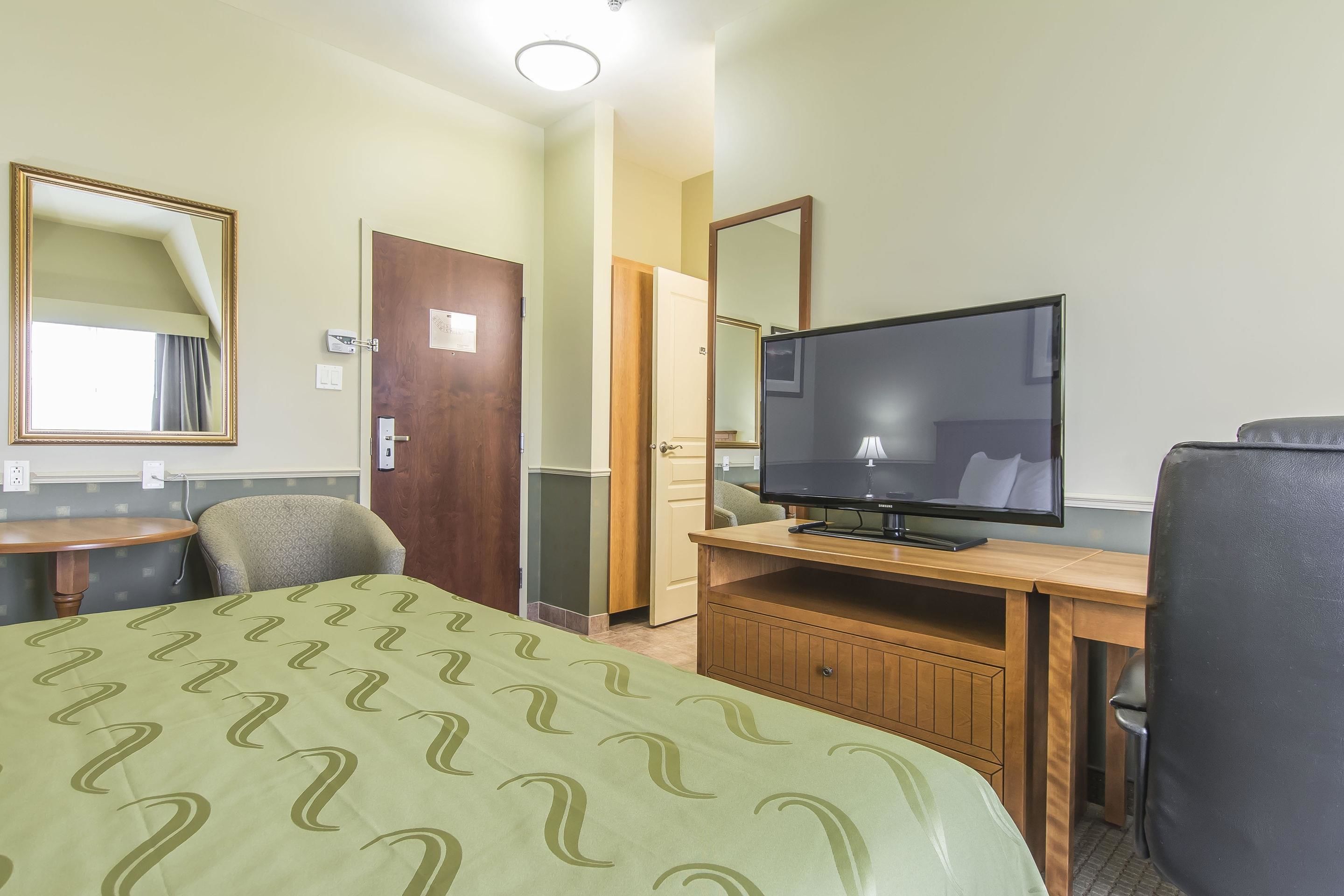 Una habitació d'hotel amb un llit, un escriptori, una televisió, una cadira i una porta.