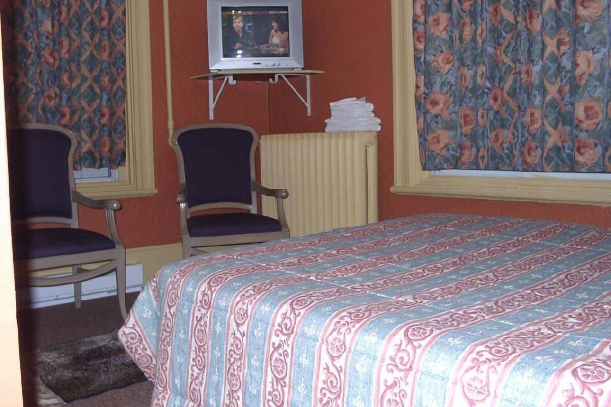 Una habitación de hotel con una cama, dos sillas, un televisor sobre un mueble bajo y cortinas con estampado floral.