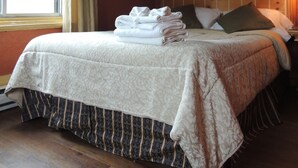 A neatly made bed with a folded white towel, a headboard with a grid pattern, a framed picture on the wall, and a window with curtains. - Hotel Arena Palace Montreal (Montreal)