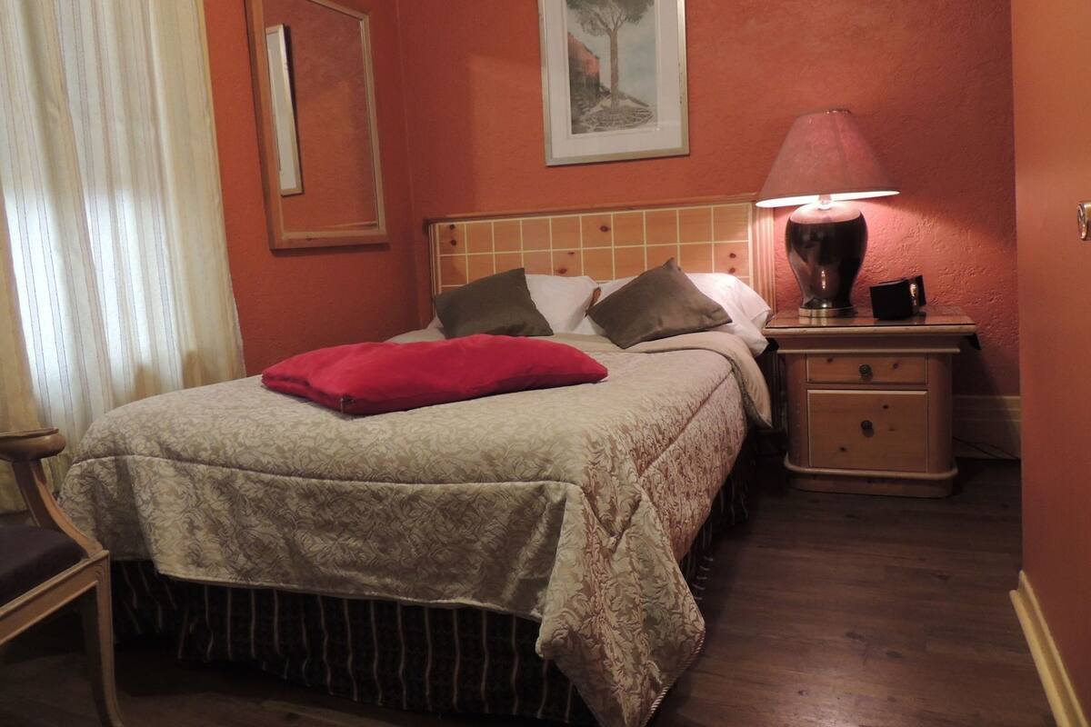 Una habitación de hotel con cama, mesita de noche, lámpara y un cuadro en la pared.