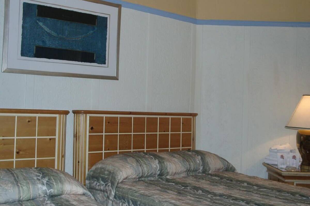 Un dormitorio con dos camas, un cuadro enmarcado en la pared y una mesita de noche con una lámpara.
