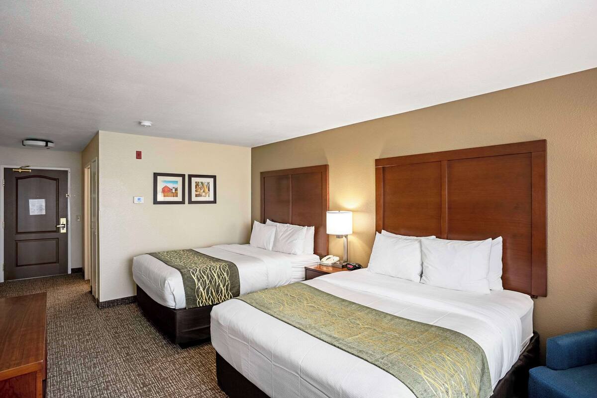 A hotel room with two beds, a desk, a chair, a lamp, and a door.