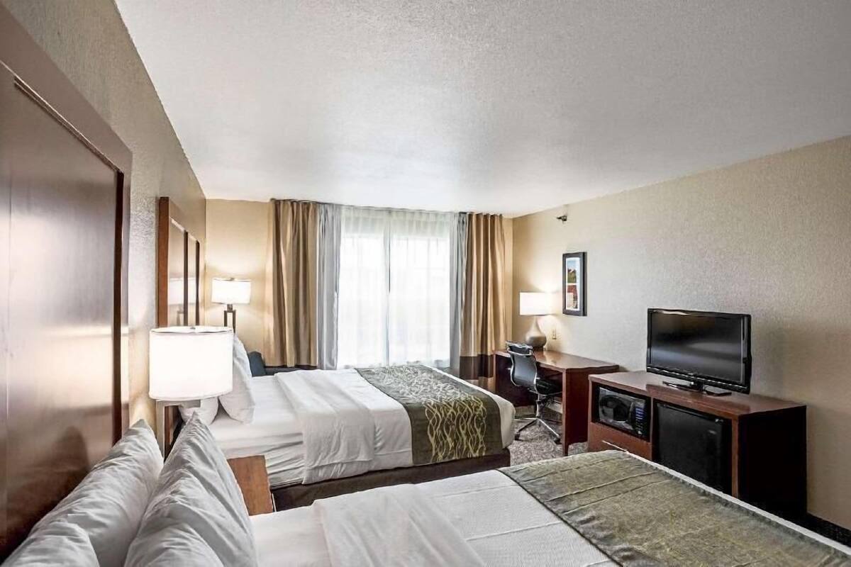 A hotel room with two beds, a desk, a television, and a window with curtains.