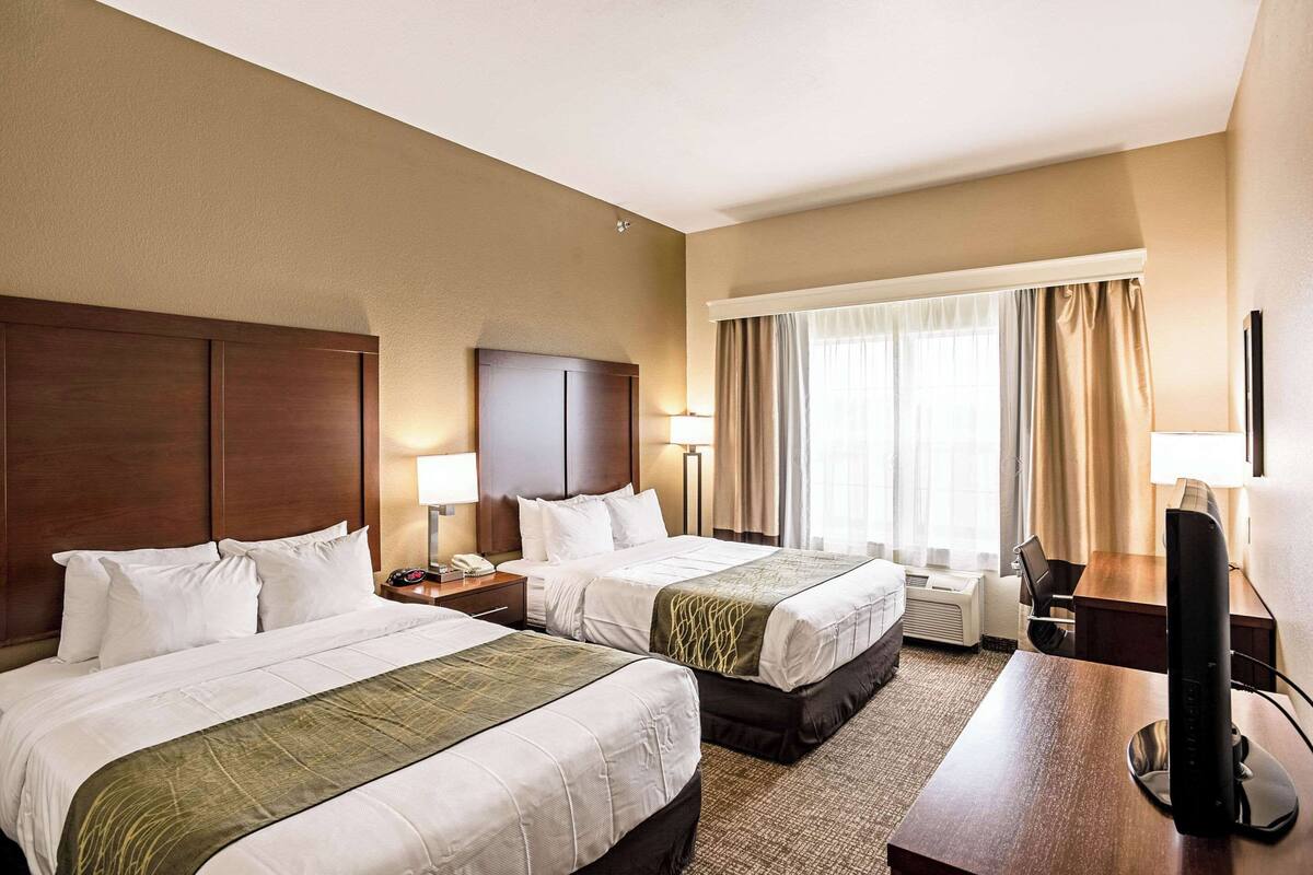 A hotel room with two beds, a desk, a chair, a TV, and a window with curtains.