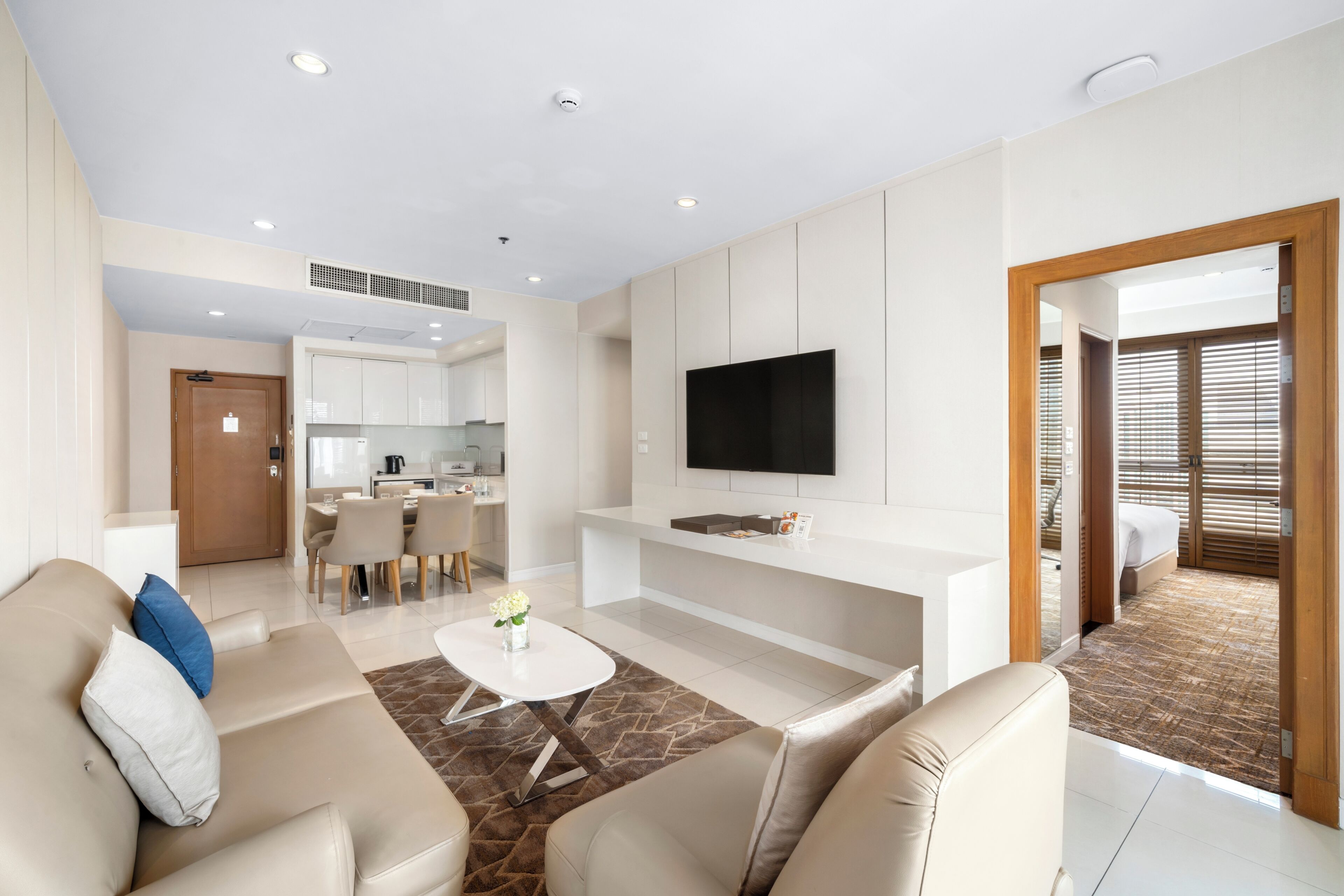 A modern living room with a flat-screen TV, a sofa, a coffee table, and a dining area.