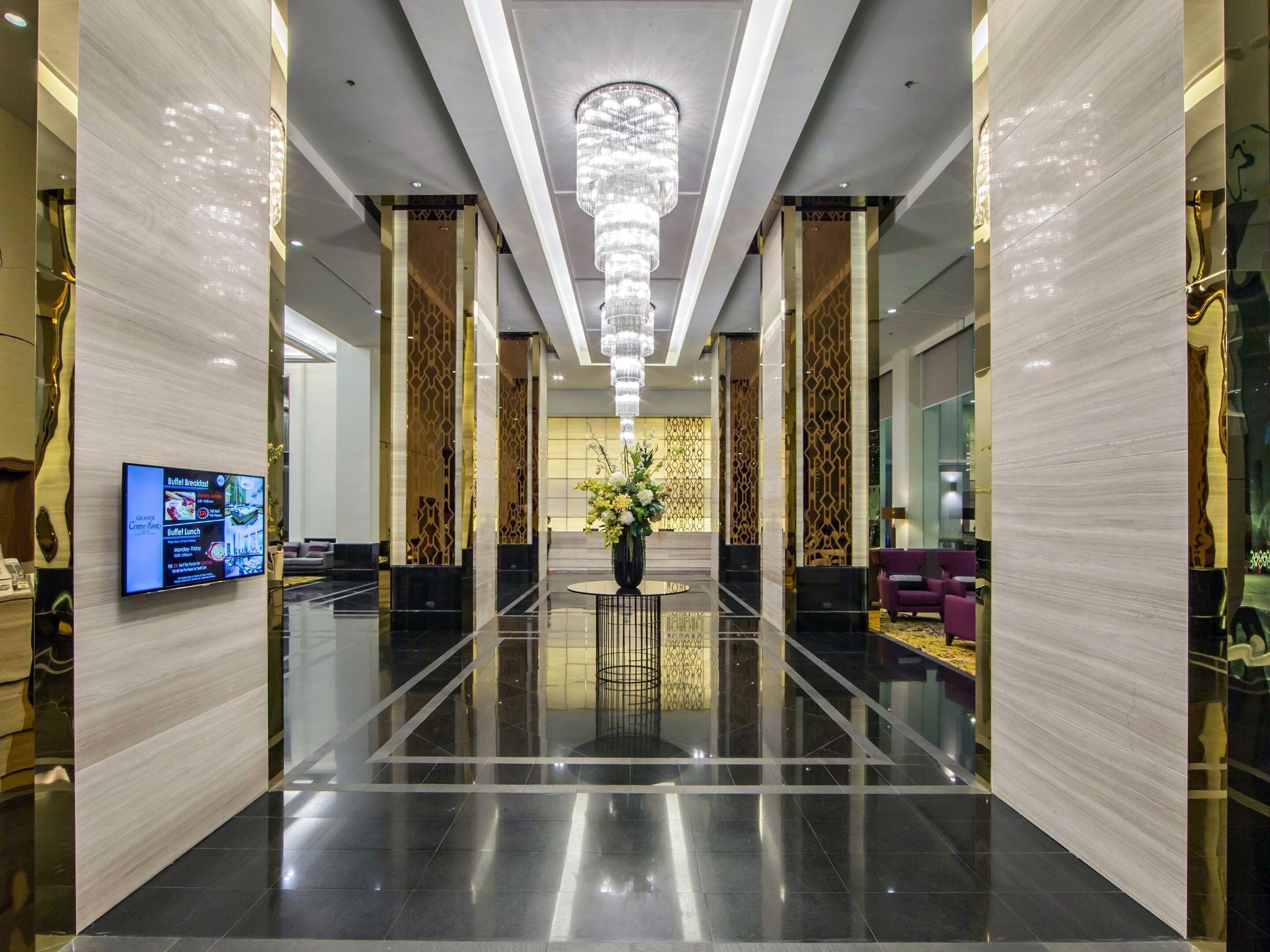 Een moderne hotellobby met een glanzende zwarte vloer, een kroonluchter in het midden en een zithoek met paarse banken.