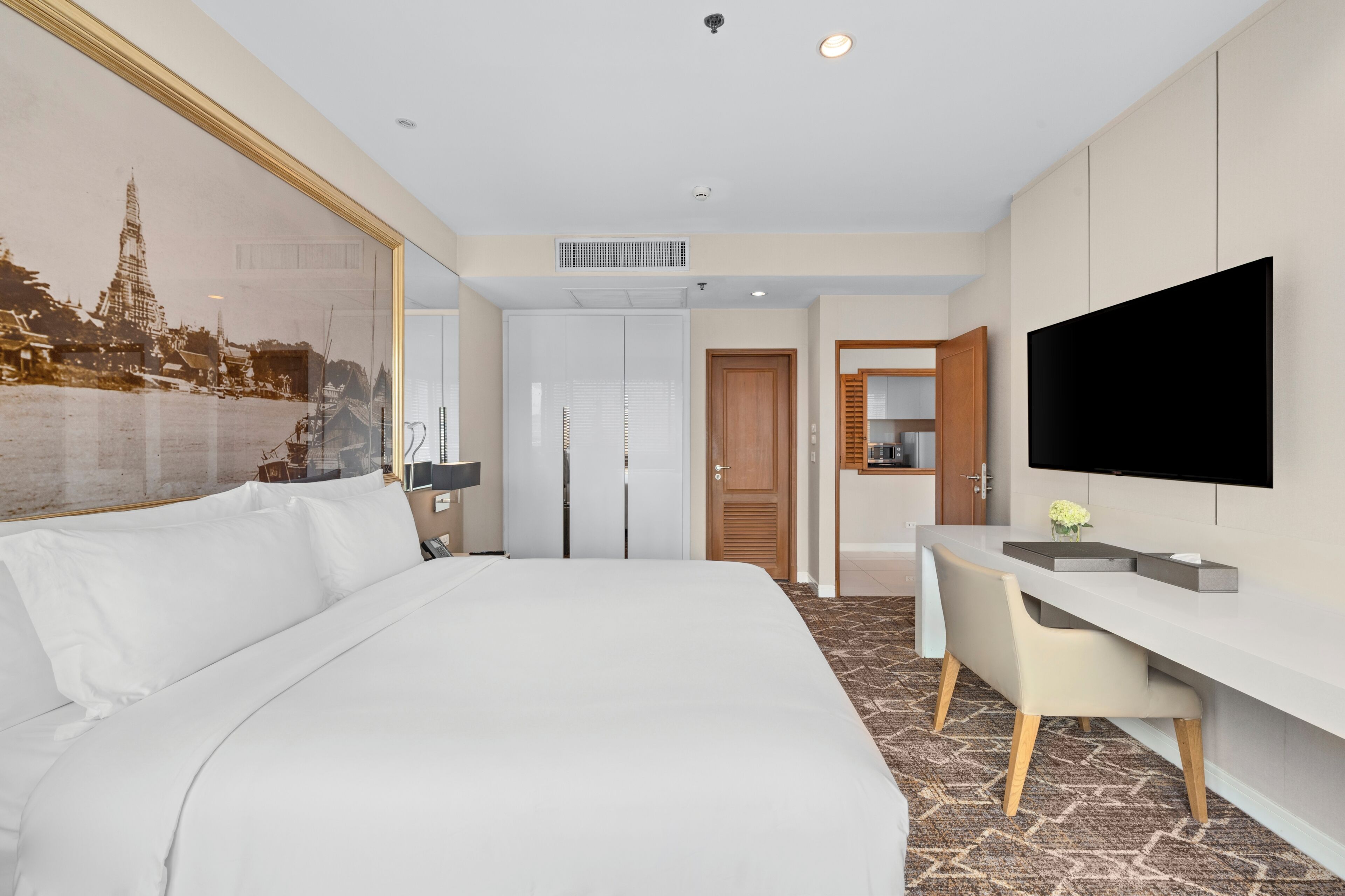 A hotel room with a large bed, a desk, a TV, and a view of a temple through the window.