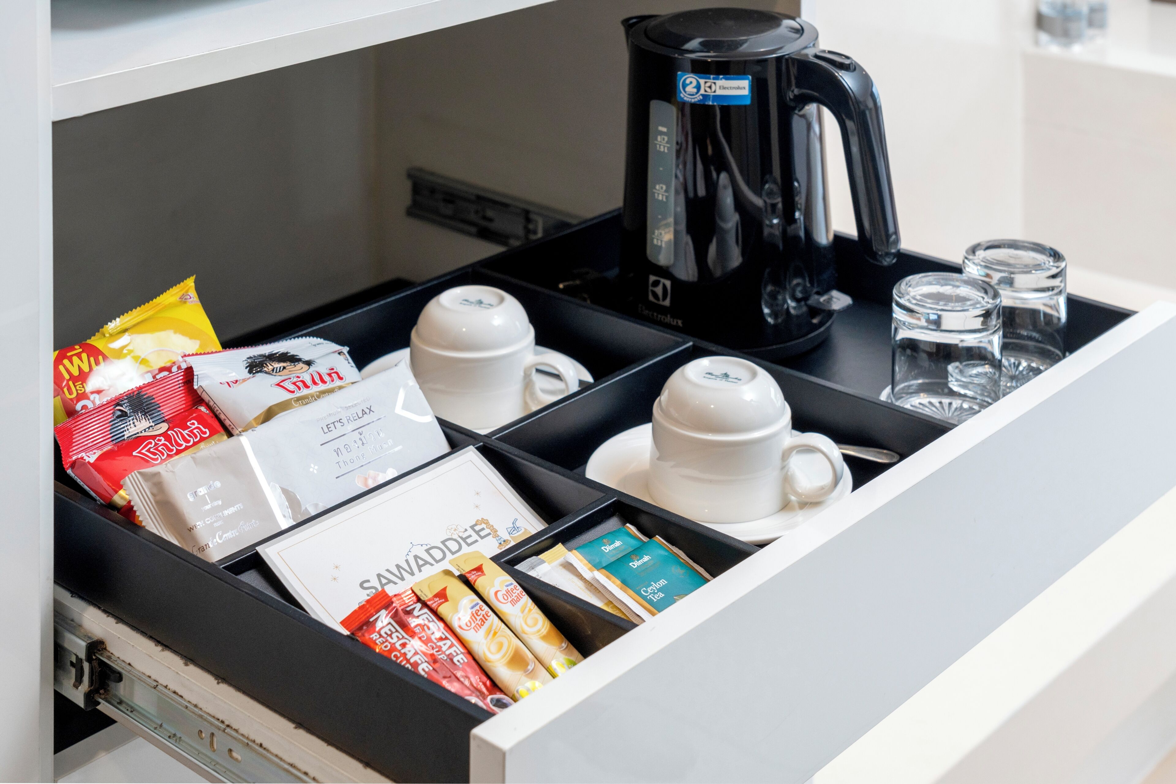 A drawer with a coffee maker, cups, and coffee packets.