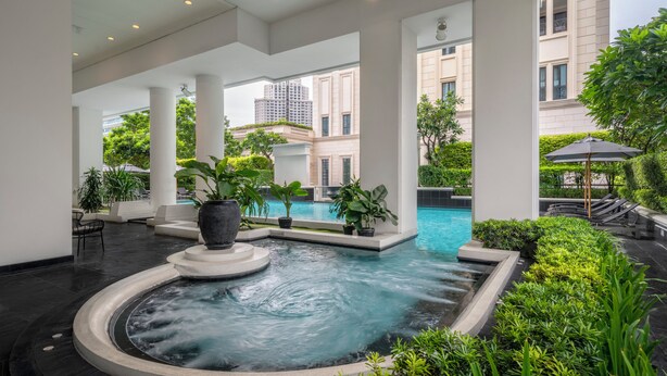 A modern indoor pool area with a central hot tub, surrounded by lush greenery and white columns. - Grande Centre Point Ploenchit (Bangkok)