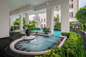 Un área de piscina interior moderna con un jacuzzi central, rodeado de exuberante vegetación y columnas blancas.