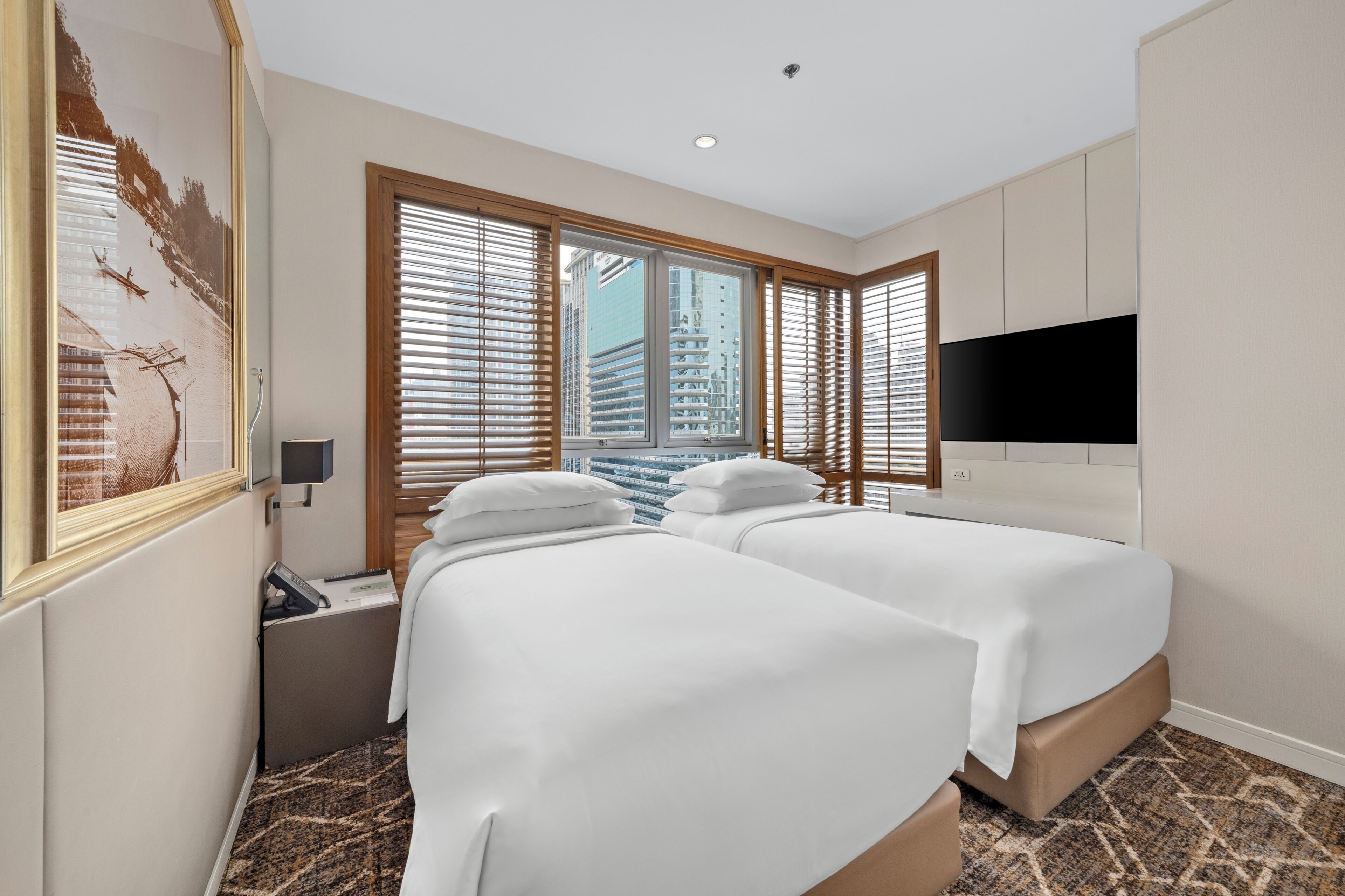 Habitación de hotel con dos camas, un televisor, una ventana con persianas y un cuadro en la pared.