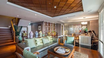 A spacious living area with a wooden ceiling, a sofa set, a coffee table, and a dining area with chairs and a table.