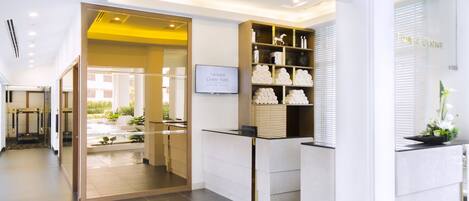 Zona de recepción de hotel con diseño moderno, que incluye un mostrador de recepción, un panel de vidrio y una exhibición de artículos de aseo.