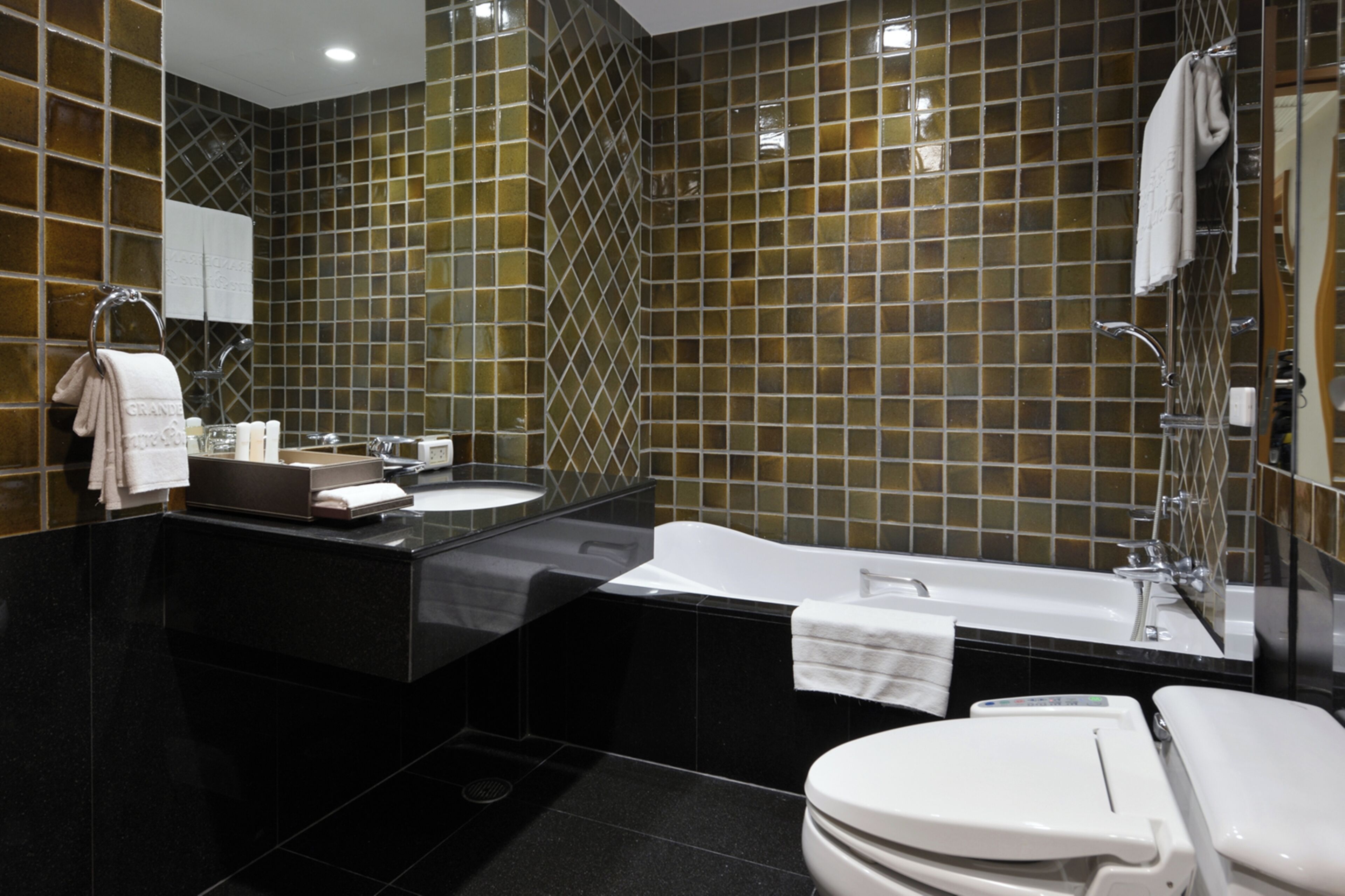 A modern bathroom with a black countertop, a white bathtub, and a white toilet.