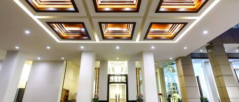 A modern hotel entrance with a geometric ceiling design, large columns, and a central doorway.