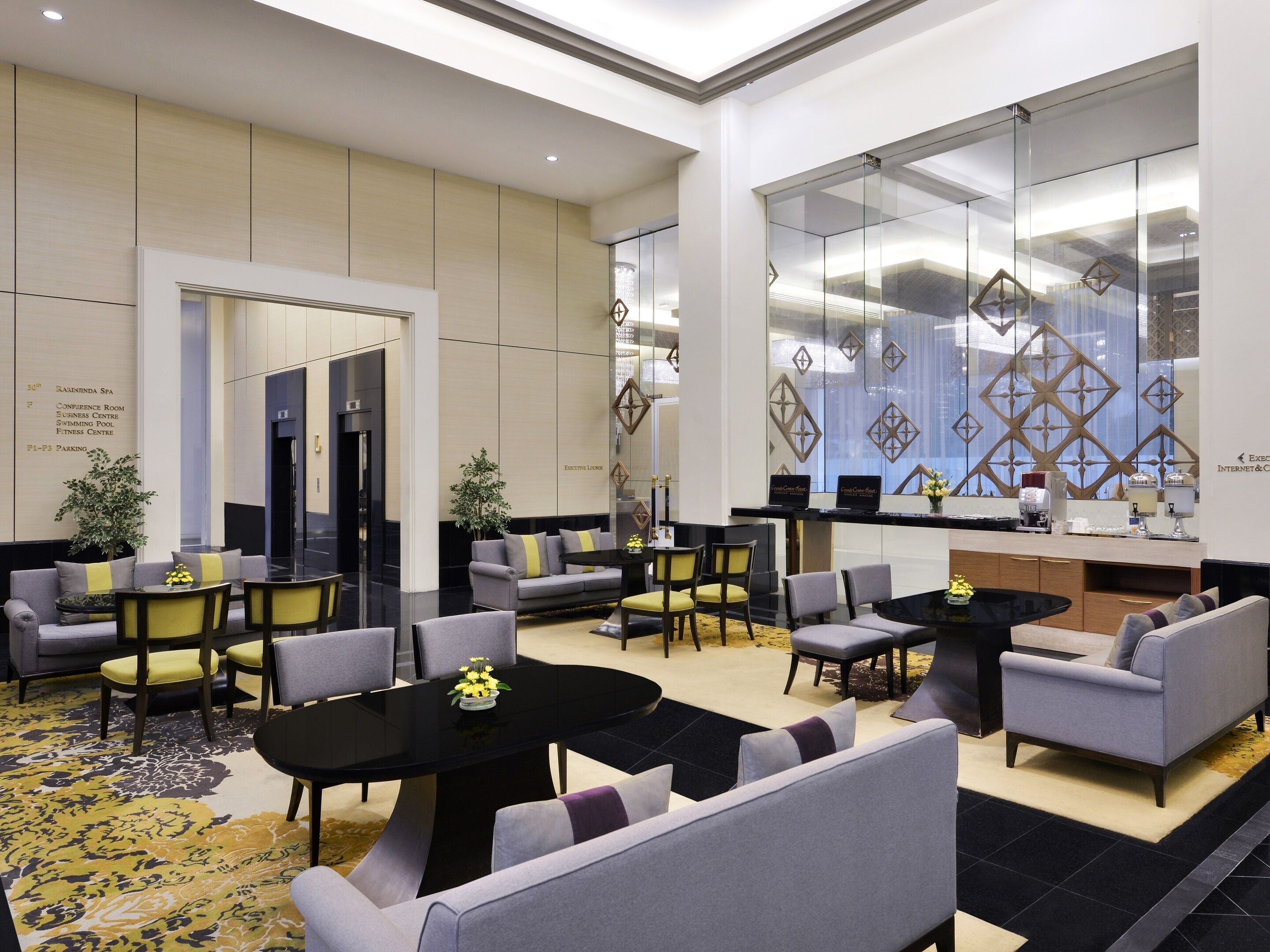 Eine moderne Hotelhalle mit Sitzbereichen, einem Empfangstisch und einer großen Glaswand mit geometrischen Mustern.