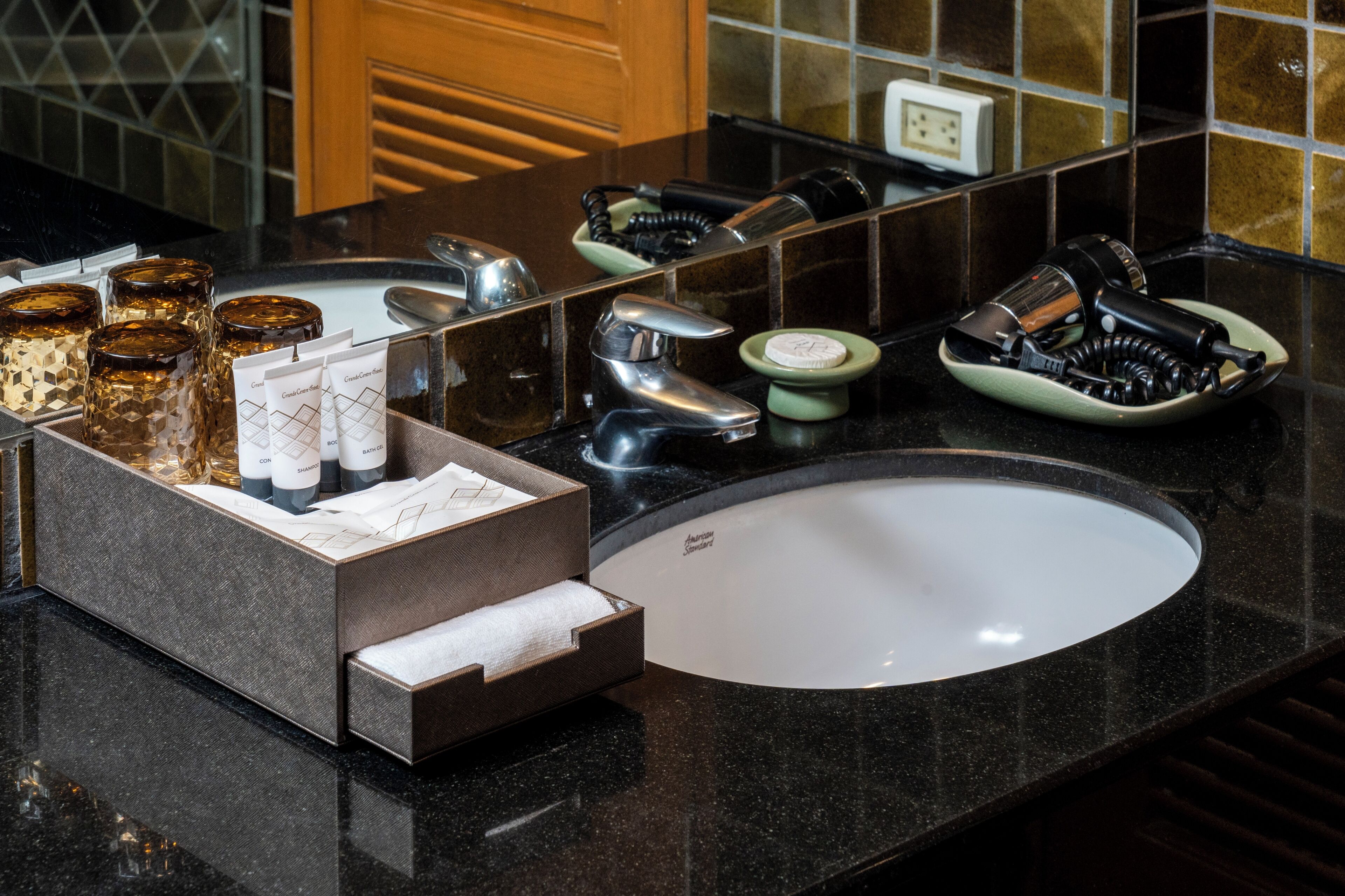 A bathroom with a black countertop, a white sink, and various toiletries including a hairdryer, a bottle of shampoo, and a soap dish.
