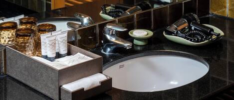 A bathroom with a black countertop, a white sink, and various toiletries including a hairdryer, a bottle of shampoo, and a soap dish.
