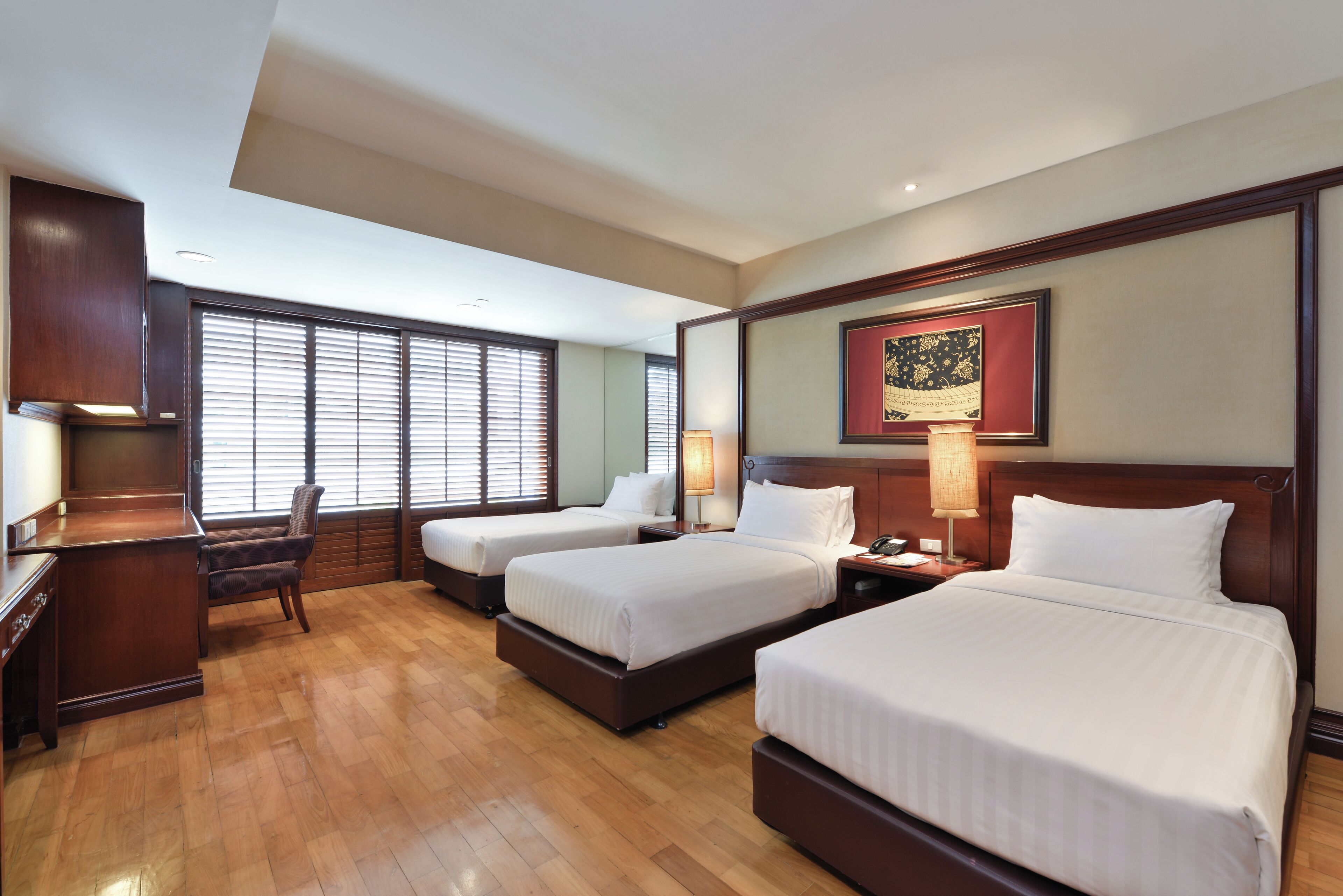 A hotel room with two beds, a desk, a chair, and a large window with blinds.