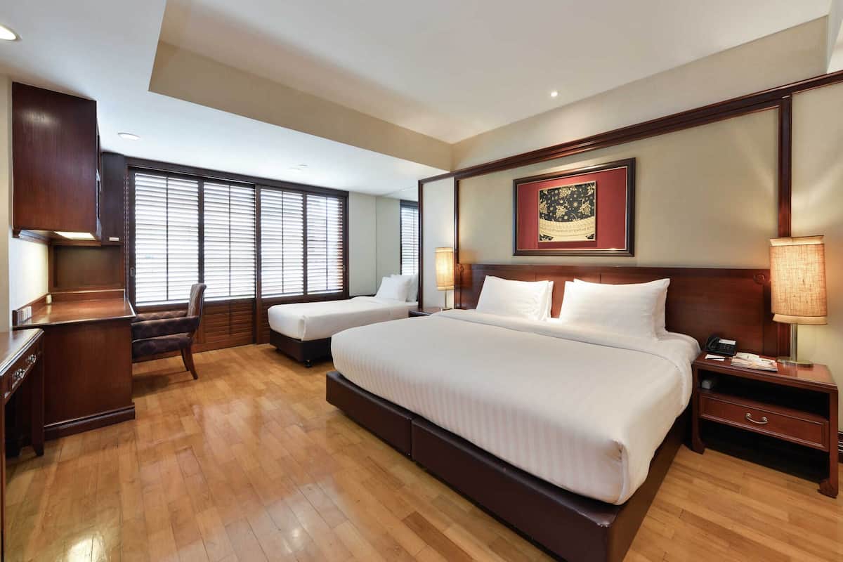 A hotel room with a large bed, two bedside tables, a desk, a chair, and a window with blinds.