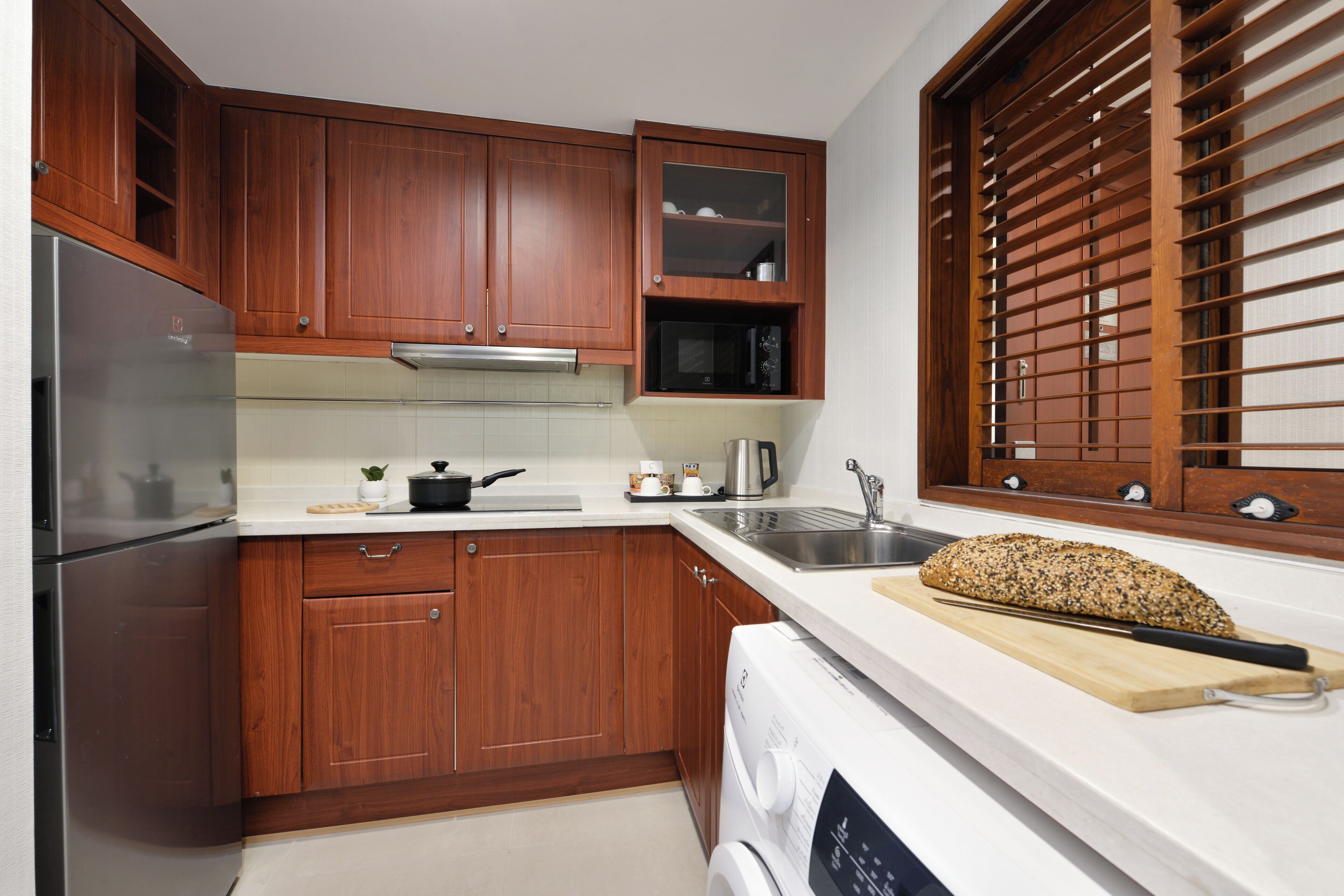 A kitchen with wooden cabinets, a stainless steel refrigerator, a microwave, and a bread loaf on the counter.