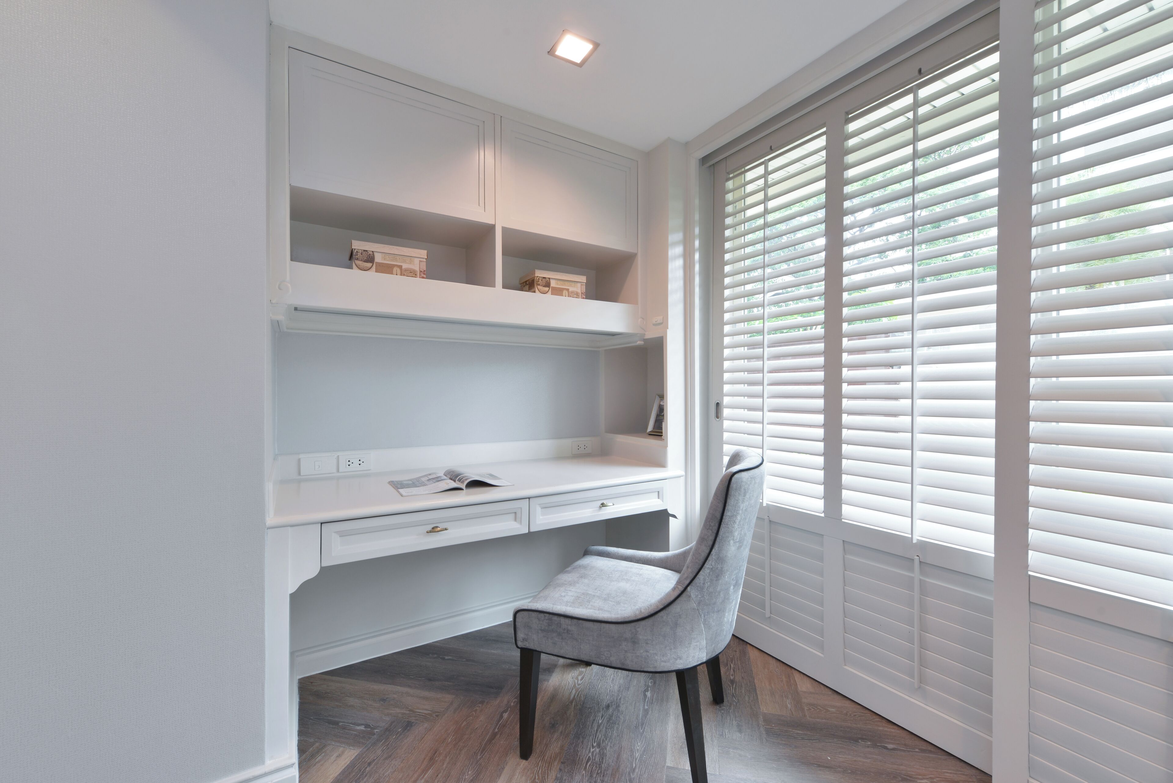 A modern study with a white desk, grey chair, and built-in shelving.
