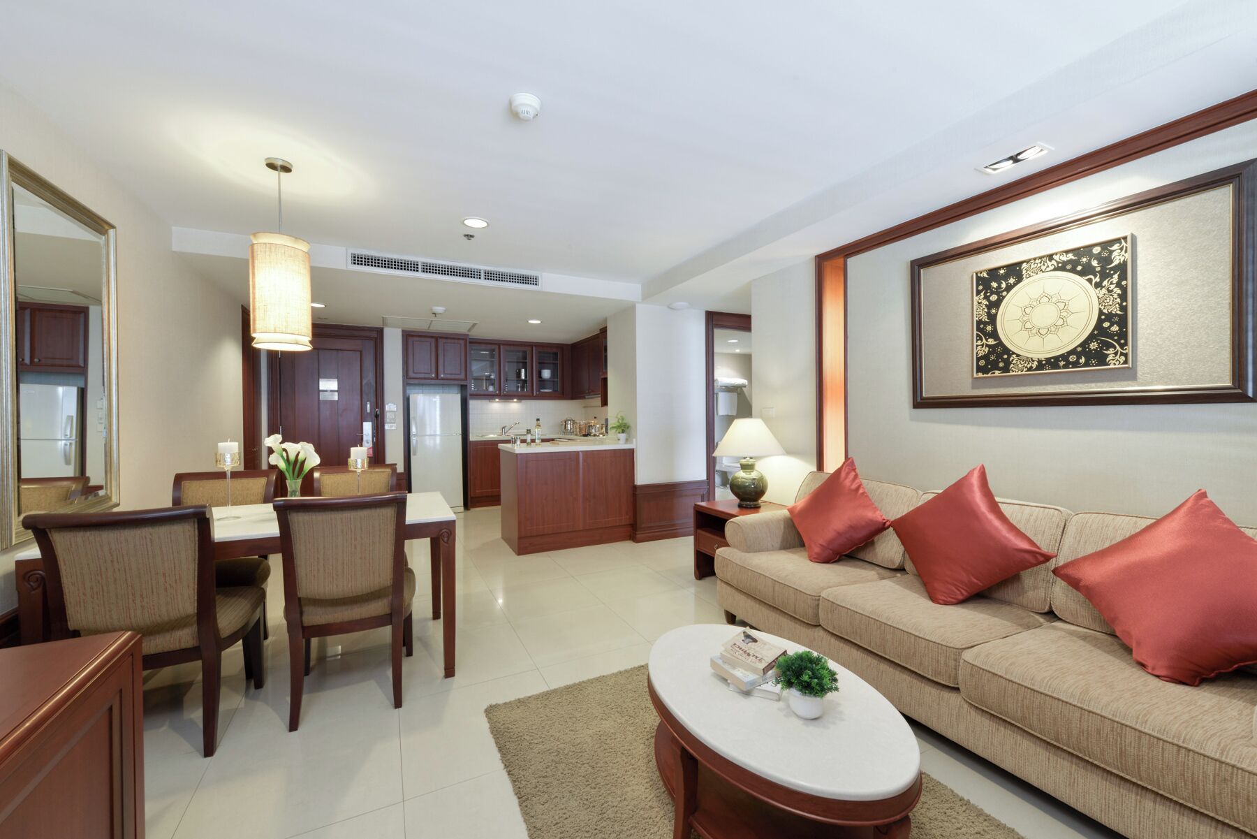 A modern living room with a beige sofa, red cushions, a coffee table, and a dining area with wooden chairs and a table.