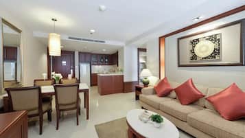 A modern living room with a beige sofa, red cushions, a coffee table, and a dining area with wooden chairs and a table.