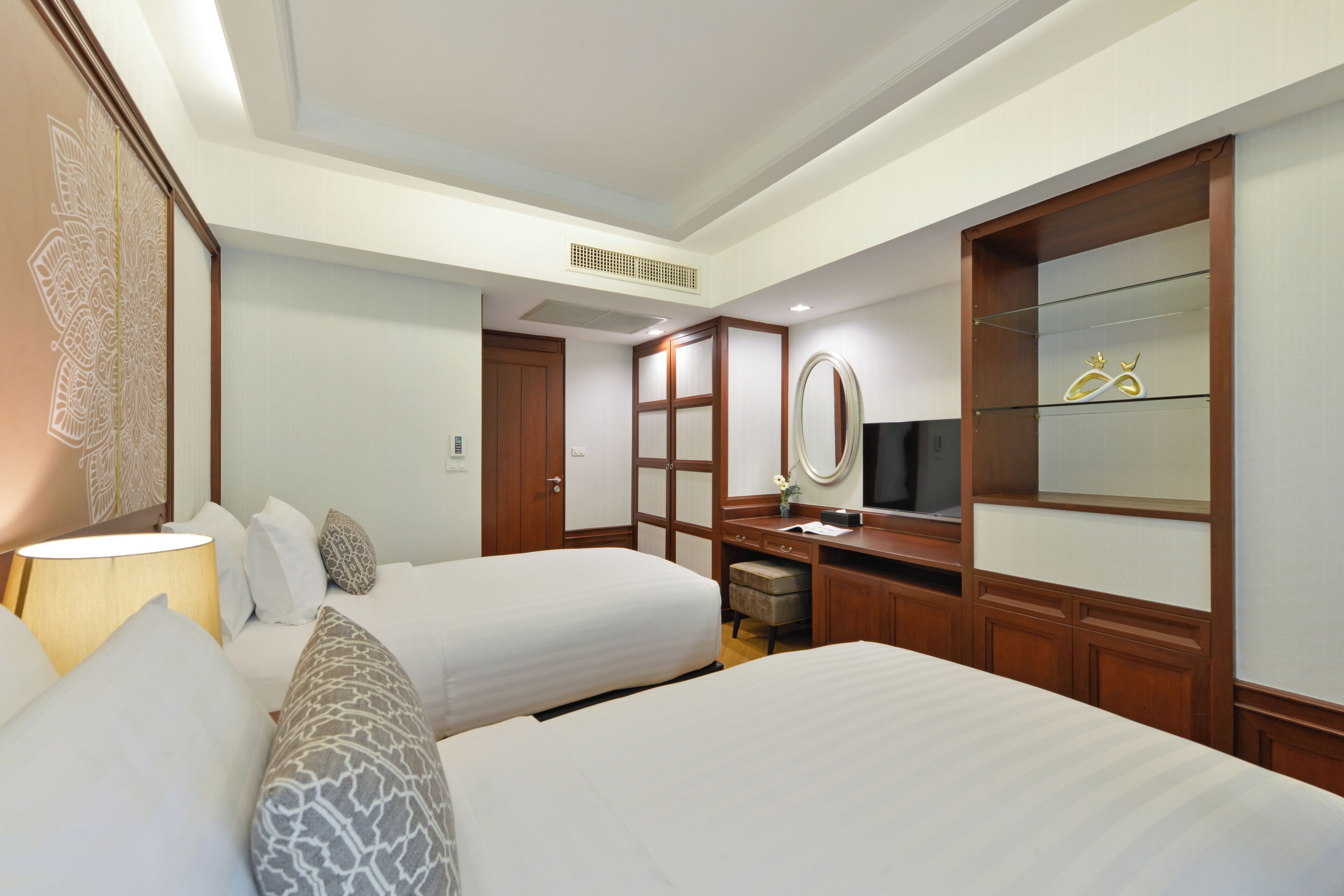 A hotel room with two beds, a desk with a mirror, a television, and a wardrobe.