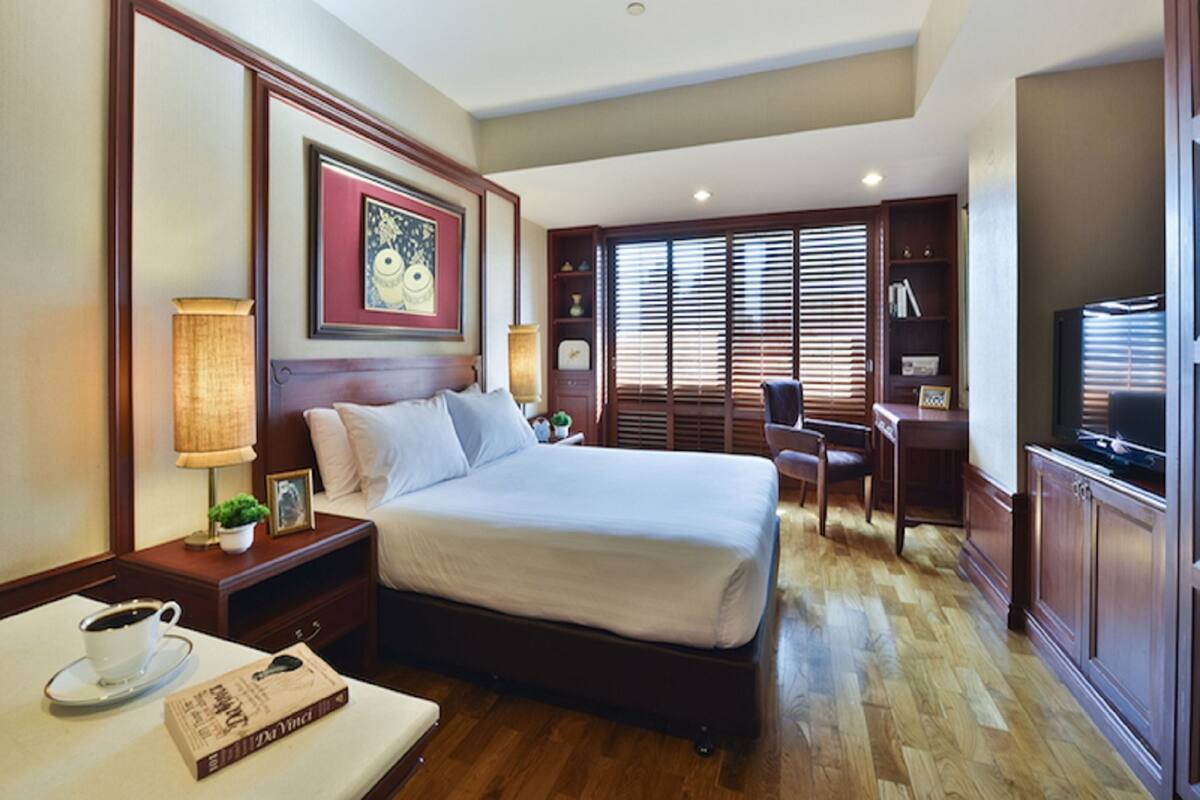 A hotel room with a large bed, a desk, a chair, a television, and a window with blinds.