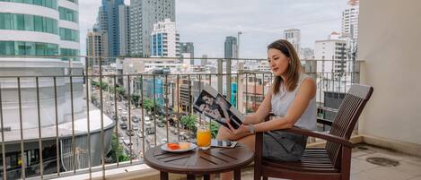 Una persona sentada a una mesa redonda con una bebida y un plato de comida en un balcón con vista a la ciudad.