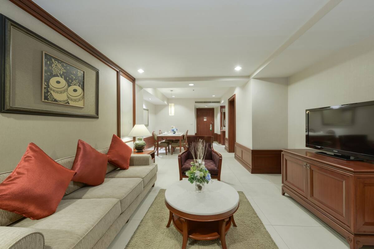 A modern living room with a sofa, a coffee table, a TV, and a dining area in the background.