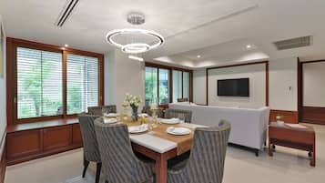 A dining area with a wooden table set for six, surrounded by upholstered chairs. There is a sofa and a small wooden side table in the background.