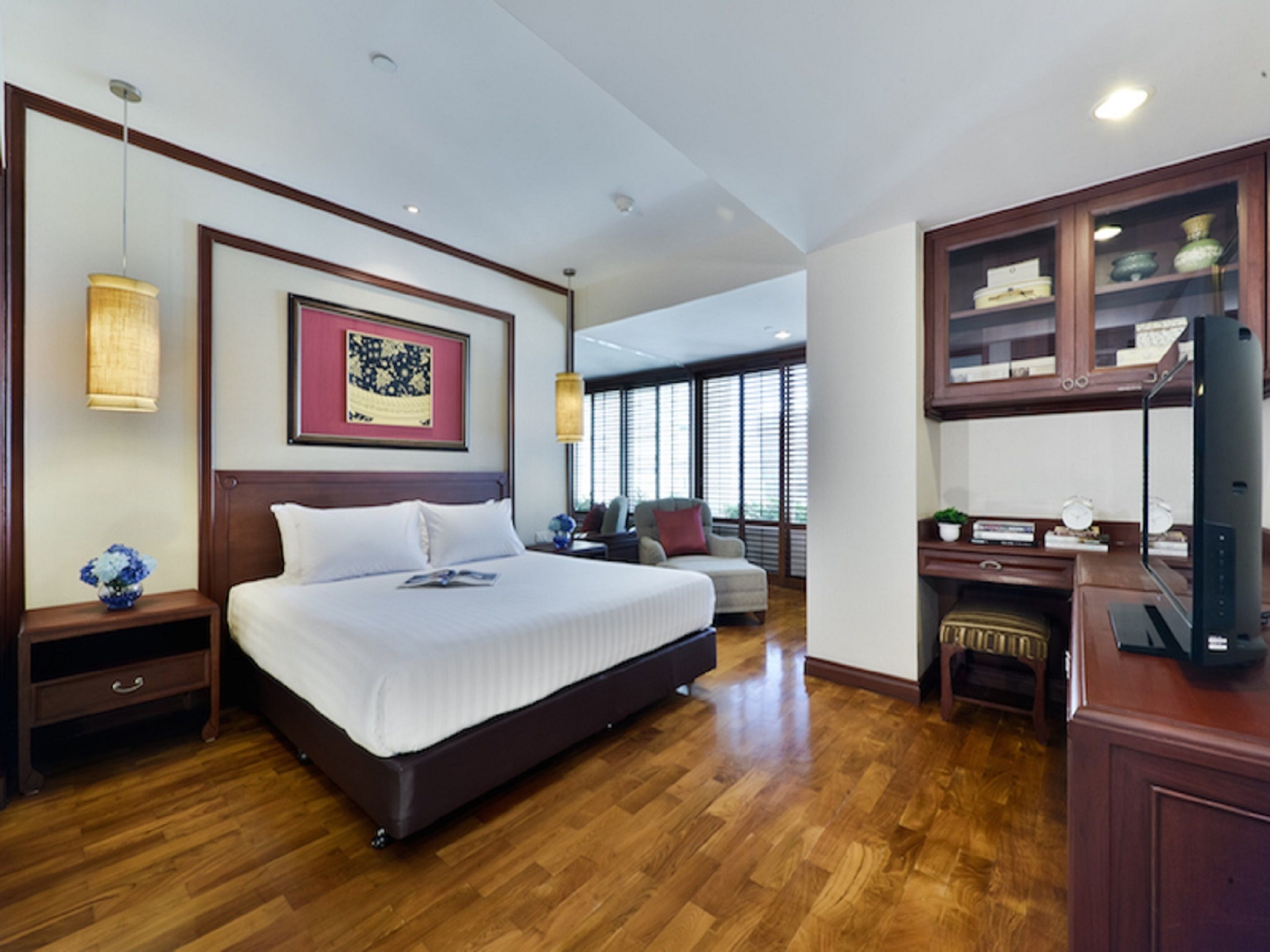 Een ruime hotelkamer met een groot bed, houten vloeren, een bureau met een computer en een televisie.