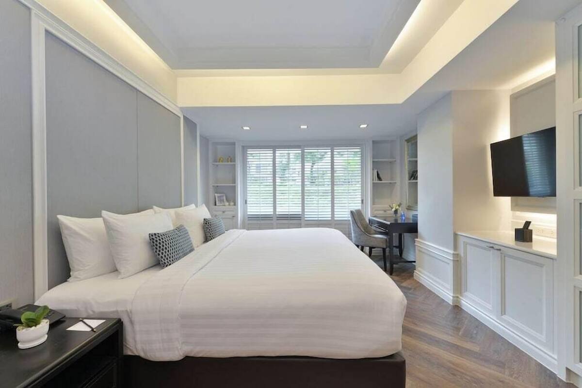 A bedroom with a large bed, bedside tables, a desk, and a TV.