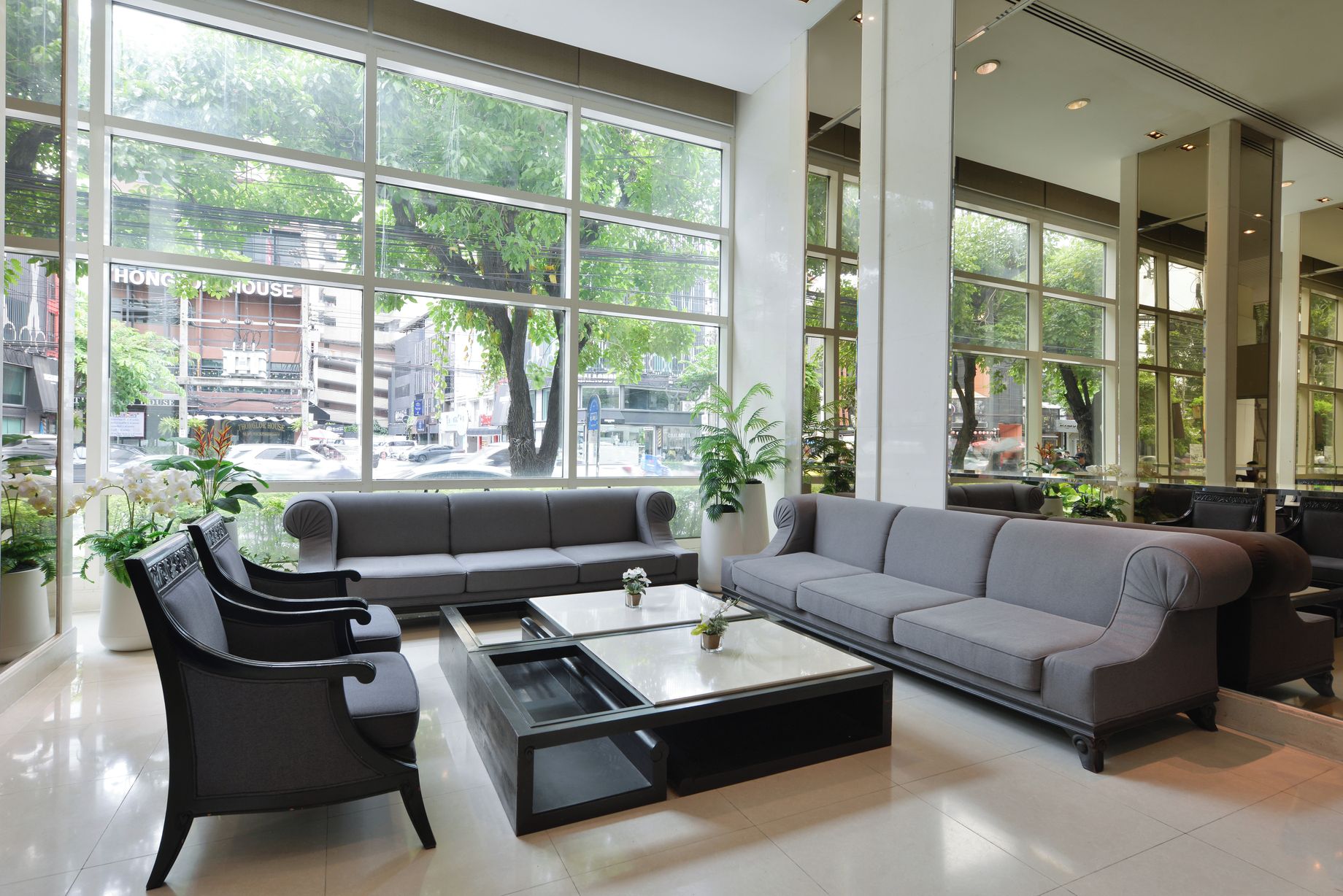 A modern hotel lobby with large windows, a grey sofa, black chairs, and a coffee table.