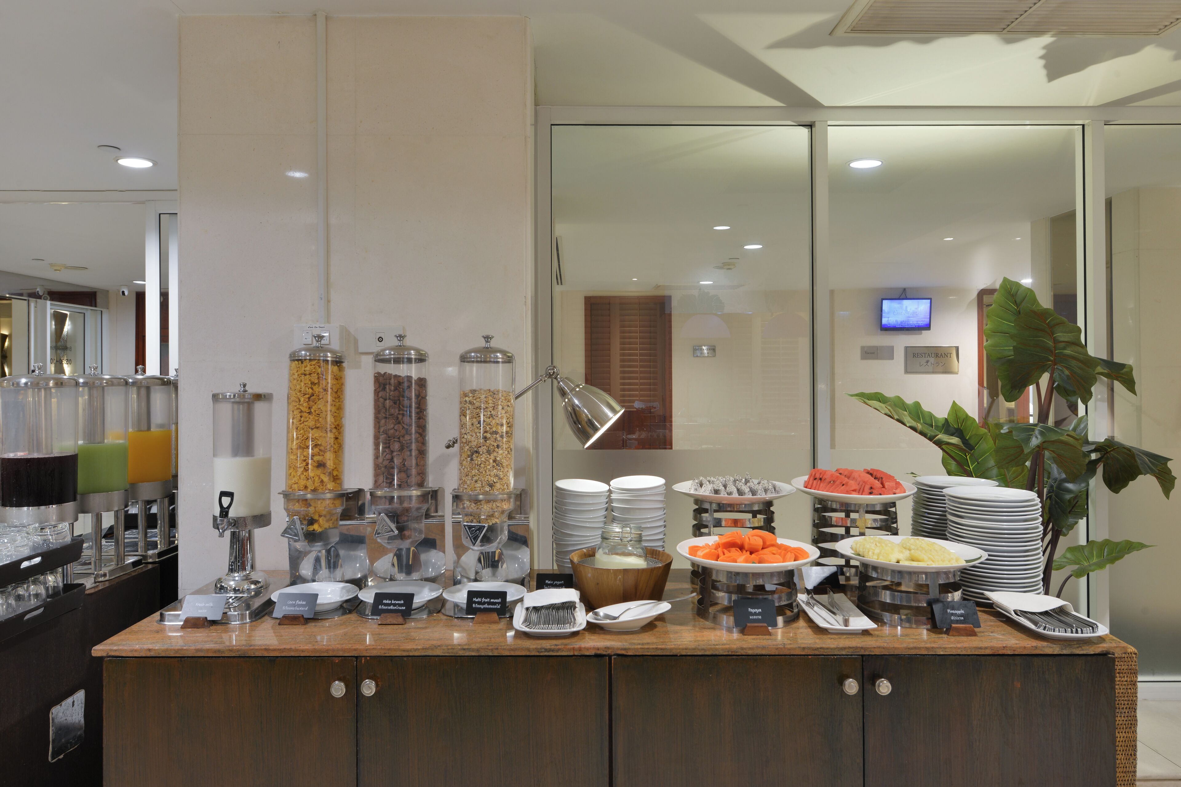 A buffet setup with various food items and serving utensils, including a coffee station and a fruit bowl.