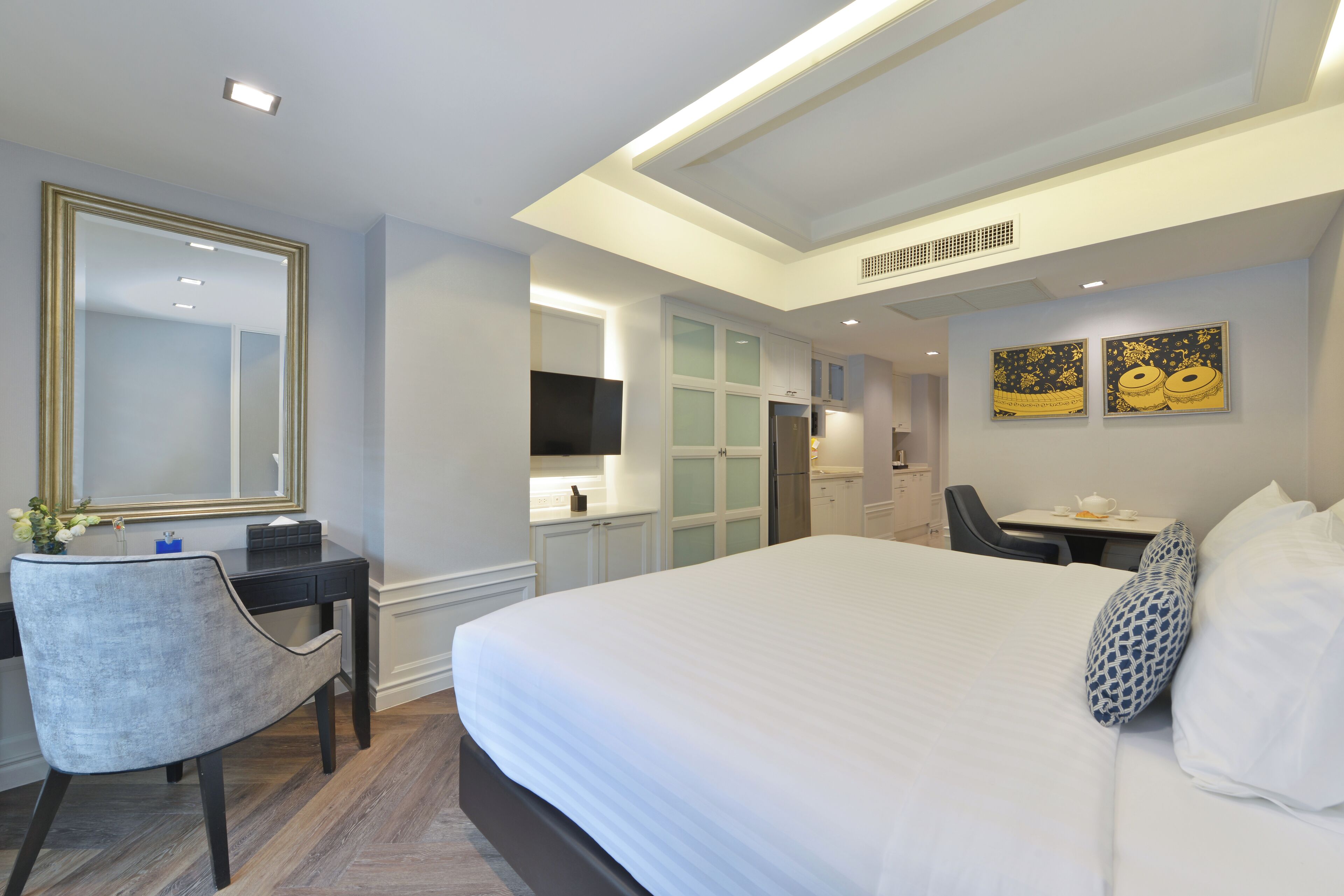 A modern hotel room with a large bed, a desk with a chair, a television, and a small table with a cup and saucer.