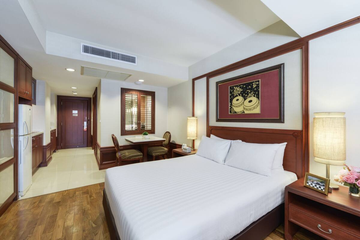 A hotel room with a large bed, a desk with a chair, a small table, and a picture frame on the nightstand.