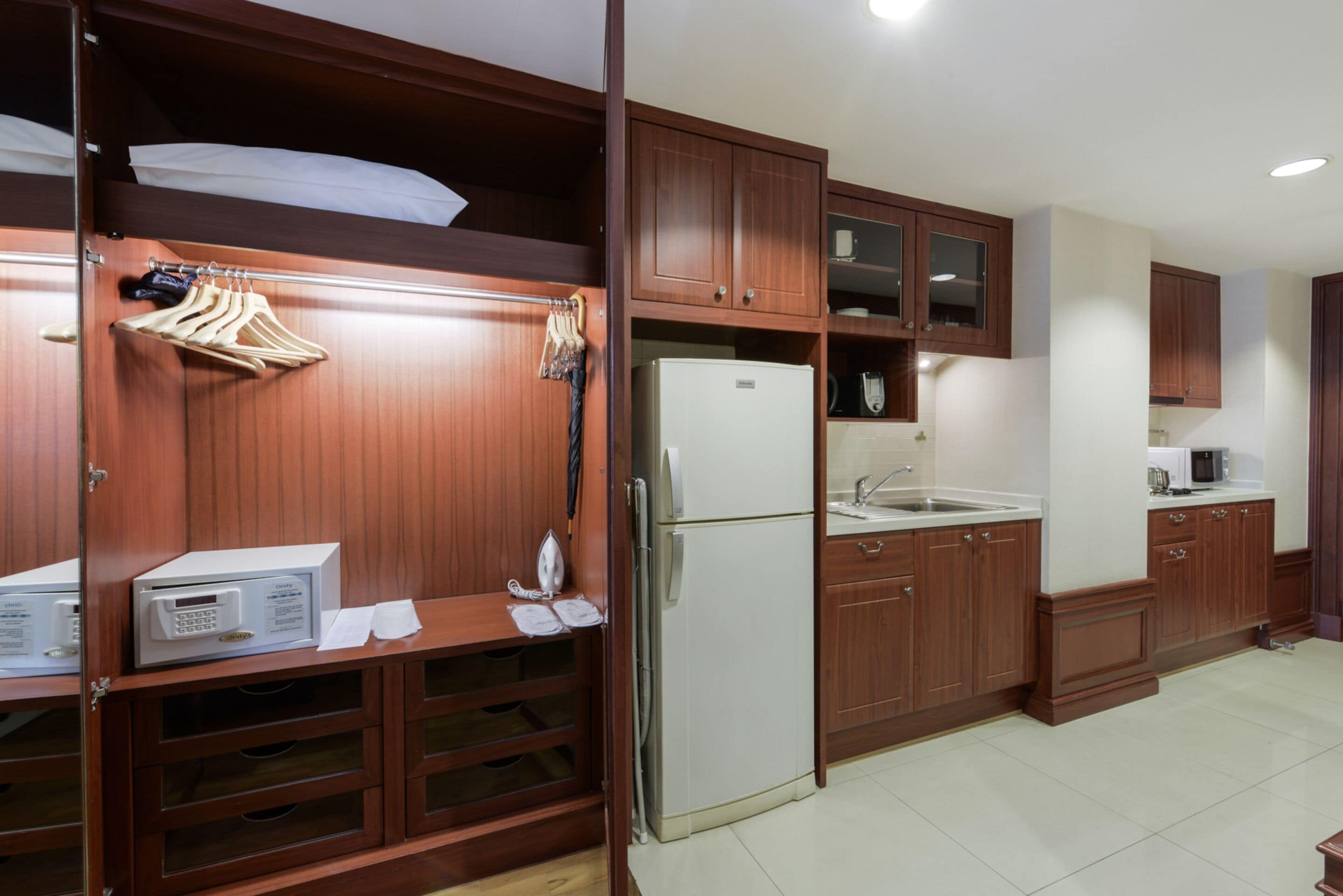 Una cocina compacta con armarios de madera, un microondas integrado, un refrigerador y un lavamanos.