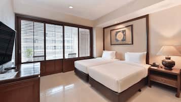 A hotel room with two beds, a desk, a chair, a TV, a framed picture on the wall, and a window with blinds.