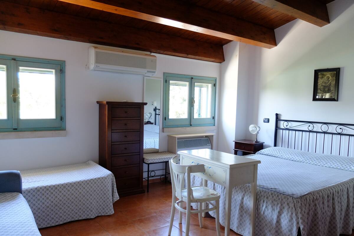 A bedroom with two beds, a desk, a chair, a dresser, and a window with shutters.