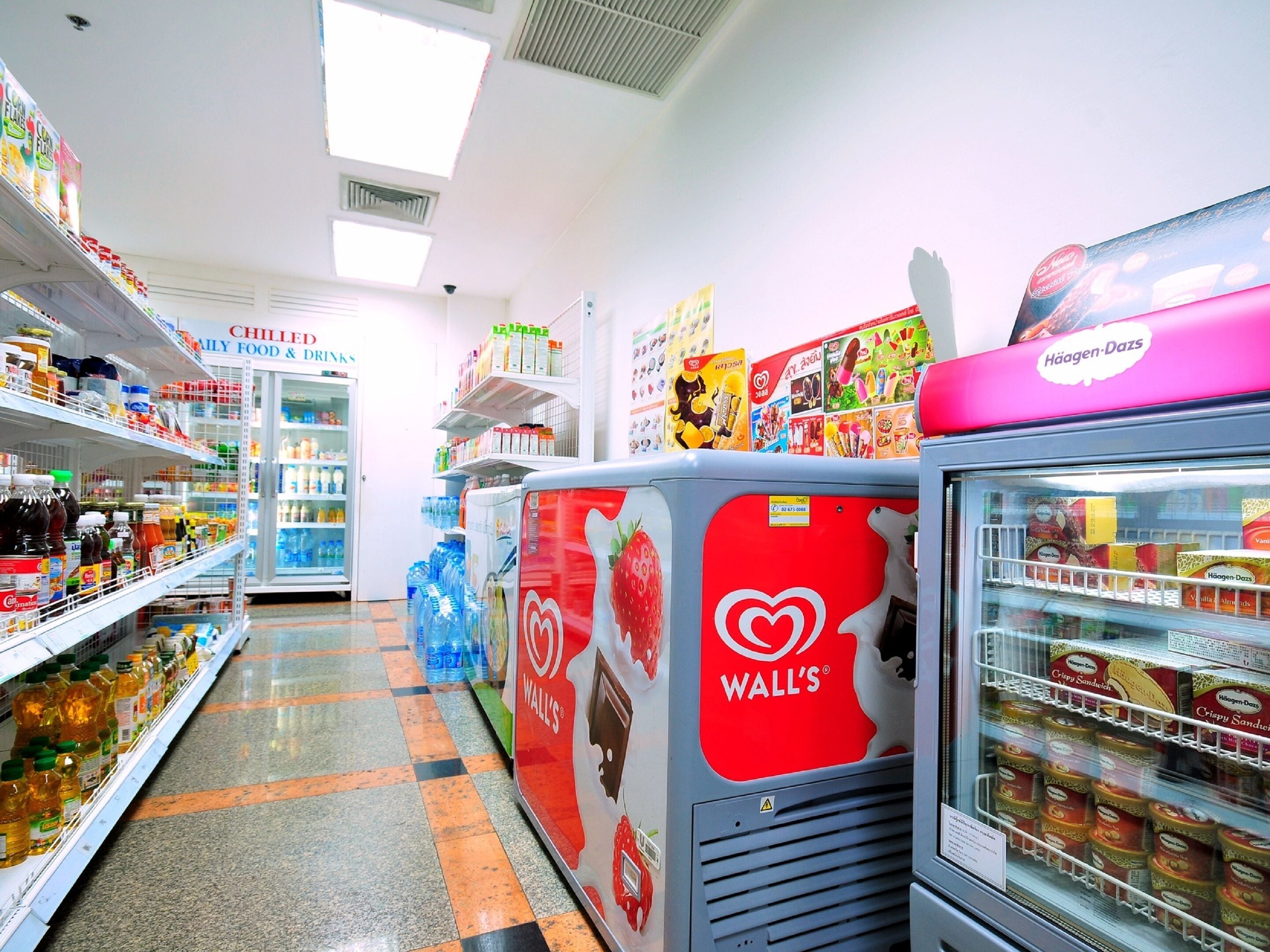 Un pasillo de supermercado con sección de alimentos y bebidas refrigerados, un refrigerador WALL'S y diversos productos alimenticios en estantes.